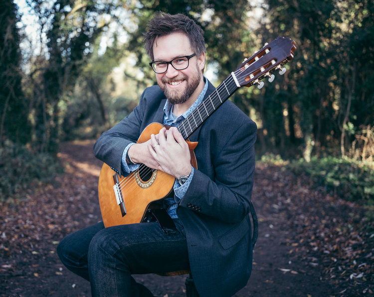 Cliff Ward smiling with a classical guitar outdoors